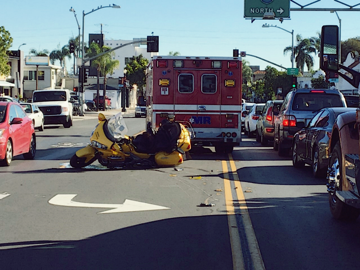 A motorcycle on the ground after an accident with an ambulance in behind it